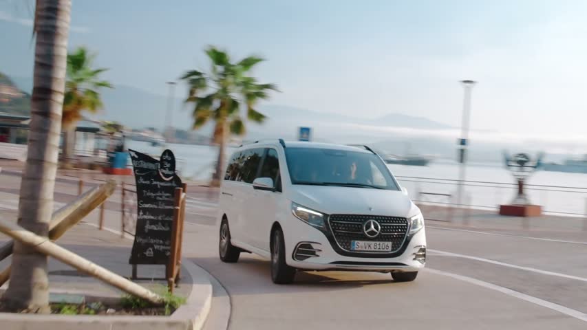 A Mercedes-Benz V-Class on a palm-lined coastal road.
