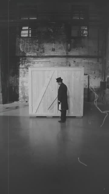 Black-and-white film still with a figure beside a wooden crate.